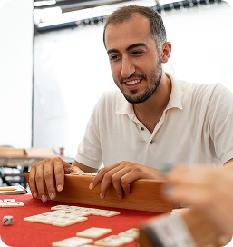 Um homem sorridente está sentado à mesa vermelha e joga um jogo de tabuleiro com fichas