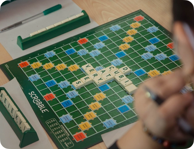 Vista do tabuleiro de Scrabble, do ponto de vista do jogador, com palavras dispostas sobre uma mesa de madeira